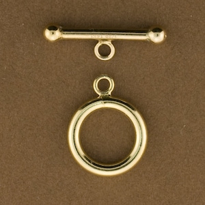 May include: Gold-toned metal toggle clasp with a round ring. The toggle has a bar with a round end and a loop on the top. The ring has a loop on the top.
