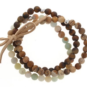 May include: A triple-strand bracelet with brown, beige, and green beads. The bracelet is tied with a brown leather cord.