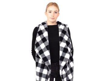 Könnte beinhalten: Eine schwarz-weiß karierte Weste. Die offene Weste ist aus einem weichen, flauschigen Material gefertigt. Die Weste wird über einem schwarzen Langarmshirt und einer schwarzen Hose getragen. Der Hintergrund ist weiß.
