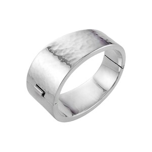 May include: A silver-colored hinged bracelet with a hammered texture on the top surface. The bracelet has a rectangular shape with rounded edges and a clasp closure. The metal reflects light, creating highlights and shadows.