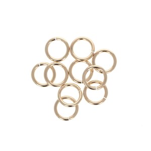 May include: A group of ten gold jump rings, all the same size, are scattered on a white background.