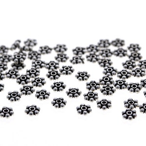 May include: A scattering of silver-toned metal beads with a flower-shaped design. Each bead has a raised center and six points around the edge.