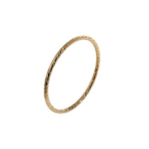 Pu&ograve; includere: Un sottile anello circolare in oro caratterizzato da una superficie testurizzata e sfaccettata che cattura la luce. La fascia presenta una larghezza costante e delicata lungo tutta la circonferenza, creando un gioiello semplice e riflettente.