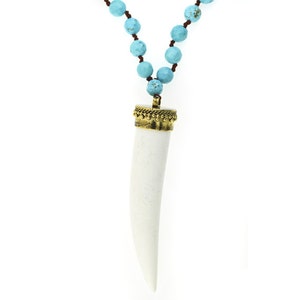 May include: A white tooth pendant necklace with a gold-toned bead trim. The necklace is made of turquoise blue beads and a brown cord.