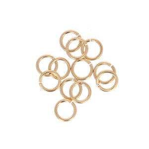 May include: A group of 10 gold jump rings, a type of jewelry finding, are scattered on a white background.