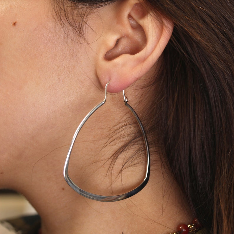 May include: Silver teardrop shaped hoop earrings. The earrings are large and dangle from the earlobe.