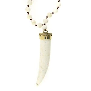 May include: A white and brown beaded necklace with a white, tooth-shaped pendant with a gold top.