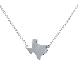 May include: A silver-colored necklace featuring a pendant in the shape of the state of Texas. The pendant is connected to a delicate chain. The necklace is displayed against a white background.