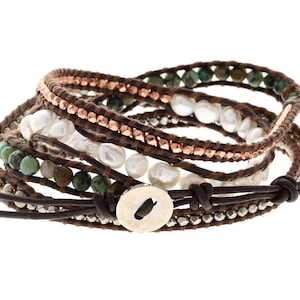 以下が含まれることがあります： ターコイズ、ゴールド、シルバーのビーズ、白いパール、銅のアクセントが付いた、マルチストランドのレザーラップブレスレット。ブレスレットは、シルバーボタンが付いたブラウンレザーの留め具が付いています。