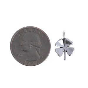 Puede incluir: Un colgante de tr&eacute;bol de cuatro hojas de plata, que se muestra junto a una moneda de veinticinco centavos de d&oacute;lar estadounidense para comparar el tama&ntilde;o.