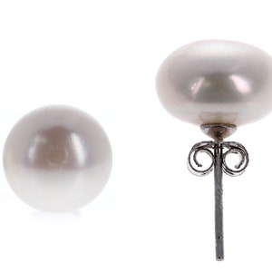 May include: A pair of stud earrings featuring round, lustrous white pearls. One earring is shown from the front, displaying the smooth, spherical surface of the pearl. The other earring is shown from the side, revealing the metal post and butterfly back.