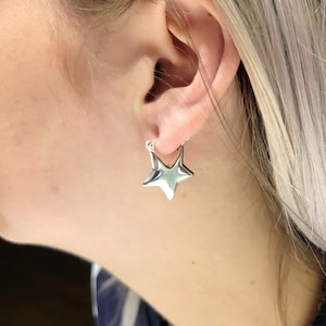 Peut inclure: Gros plan d'une boucle d'oreille argentée en forme d'étoile. La boucle d'oreille est une étoile brillante à cinq branches avec une surface lisse. La boucle d'oreille est fixée à un cerceau argenté inséré dans l'oreille.