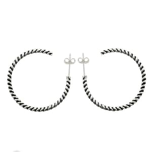 May include: A pair of silver hoop earrings featuring a twisted rope texture. Each earring is designed as an open circle with a post and butterfly back closure. The metal has a polished finish with darkened recessed areas to highlight the twist.