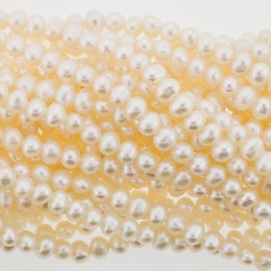 May include: A strand of white freshwater pearls, each pearl is round and smooth. The pearls are arranged in a loose pile, showing their natural lustre.