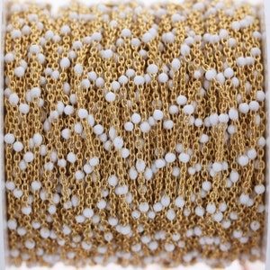May include: A spool of gold chain with white beads. The chain is made of small, linked metal pieces and the beads are evenly spaced along the chain.