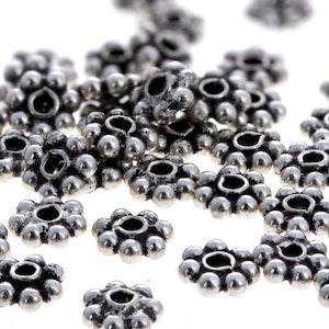 May include: A close-up of silver metal flower-shaped beads. The beads have a raised, textured design and a small hole in the center.