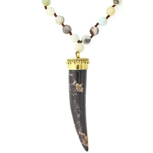 May include: A black and gold necklace with a long, black, marbled, horn-shaped pendant. The necklace is made of small, round, green, white, and brown beads.
