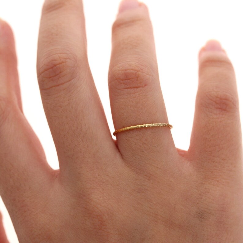 Pu&ograve; includere: Un anello d'oro sottile e delicato con una superficie testurizzata e leggermente martellata. La fascia &egrave; circolare e mantiene una larghezza sottile e costante in tutto il suo design, circondando il dito con un sottile riflesso metallico.