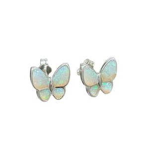 May include: A pair of butterfly stud earrings. Each earring features a silver-toned frame with a butterfly-shaped opal stone. The opal has a pearly white base with iridescent green and blue flashes. The earrings are set against a white background.