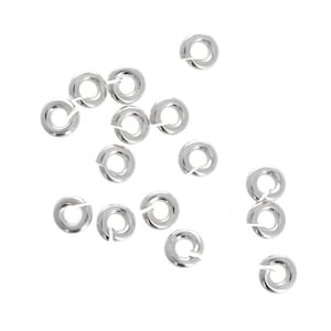 May include: A collection of silver jump rings, a type of jewelry finding used for connecting chains, cords, and other jewelry components.