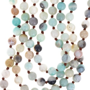 May include: A multi-strand necklace made of green, brown, and white beads. The beads are round and have a natural, polished look. The necklace is strung on brown cord.