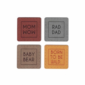 May include: Four square fabric patches with different sayings. The patches are brown, gray, and orange. The sayings are "Mom Wow", "Rad Dad", "Baby Bear", and "Born to be Wild."