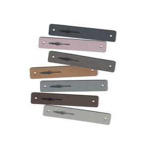 May include: Rectangular leather tags in various colors, including gray, brown, and pink. Each tag features a tree design and a hole at each end. The tags are arranged on a white background.