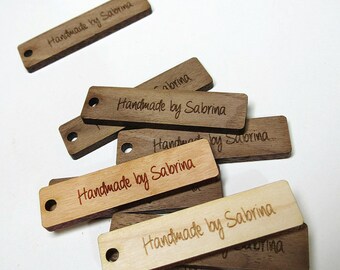 May include: A close-up of several wooden tags with the text "Handmade by Sabrina" engraved on them. The tags are various shades of brown and have a hole punched in the top for hanging.