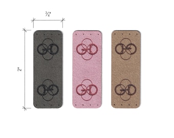 May include: Three leather labels with a repeating pattern of interlocking circles. The labels are 2 inches long and 3/4 inch wide. The labels are in gray, pink, and brown.