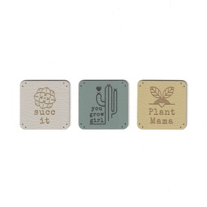 May include: Three square-shaped leather patches with different designs and text. The first patch is white with a gold succulent design and the text "succ it". The second patch is blue with a gold cactus design and the text "you grow girl". The third patch is beige with a gold plant design and the text "Plant Mama".