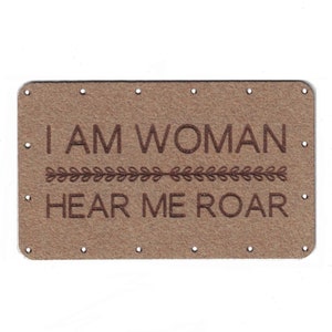 May include: Brown leather patch with the text "I AM WOMAN HEAR ME ROAR" in brown embroidery. The text is separated by a line of small leaf designs.