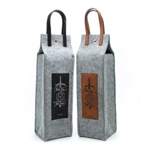 May include: Two gray felt wine bottle carriers with leather handles. One has a black leather patch with white text and a sword graphic, the other has a brown leather patch. The text reads "Have Dice Will Travel".