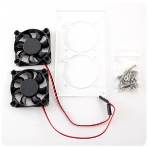 Op de afbeelding: Een computerkoelingskit van bovenaf gezien. De kit bevat twee zwarte ventilatoren, een helder acryl paneel met twee cirkelvormige uitsparingen, een zakje schroeven en rode en zwarte draden.