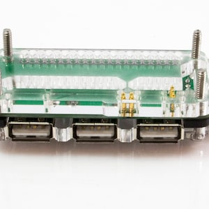 May include: A clear USB hub with a green circuit board inside. It features four USB ports and is held together with four silver screws. The hub is designed to increase the number of USB connections available.