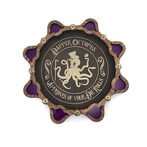 May include: A wooden dice tray with a purple inset and a gold octopus design. The octopus is wearing a top hat and holding a glass. The text around the octopus reads "Dapper Octopus Approves of Your Die Rolls".