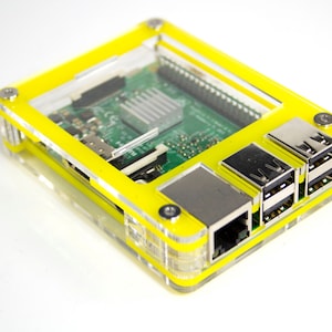 May include: A yellow clear plastic case for a Raspberry Pi computer. The case has a clear top to show the circuit board inside. The case has several ports on the side, including USB and Ethernet.