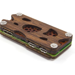 May include: A wooden Raspberry Pi case with a dark brown finish. The case has cut-out designs and is secured with silver screws. It features multiple ports and a green and brown layered design.