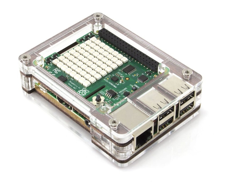 Op de afbeelding: Een transparante plastic behuizing voor een Raspberry Pi-computer. De behuizing heeft een bruine houten accent en bevat uitsparingen voor de poorten op de Raspberry Pi.