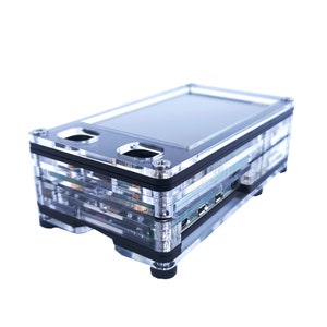 May include: A clear plastic case with a black trim, designed to hold a small computer or electronics. The case has a built-in screen and multiple ports.