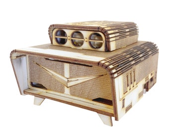 May include: A wooden model of a vintage camper van with a retro design. The camper has a white body with brown trim and a brown roof with three round windows. The camper has a distinctive fin on the back.