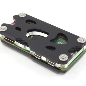 May include: A black plastic case with a circuit board inside. The case has several screws and a cutout for a chip. The circuit board has a USB connector and a micro-USB connector.