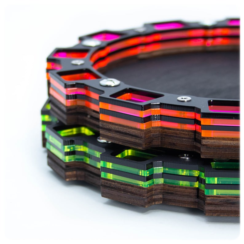Op de afbeelding: Een meerlaags houten dienblad met een zwart midden en een geometrisch ontwerp. Het dienblad heeft een gelaagd ontwerp in roze, oranje en groen rond de rand.