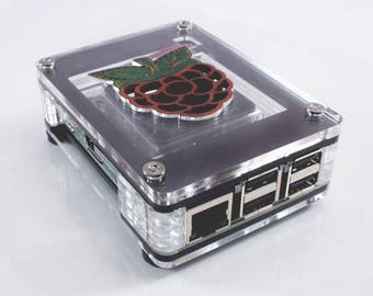 Op de afbeelding: Een transparante acryl behuizing voor een Raspberry Pi-computer. De behuizing heeft een zwarte basis en een transparante bovenkant met een frambozenlogo. De behuizing heeft een USB-poort en een ethernetpoort aan de zijkant.