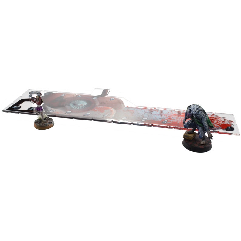 May include: A clear acrylic gaming mat with a red and white bloody design. The mat features a large eye graphic and a small skull graphic. Two miniature figures are placed on the mat.