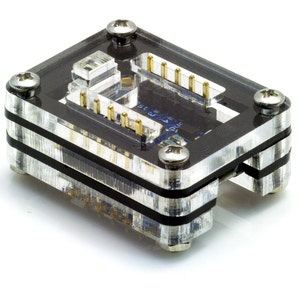 May include: A clear plastic case with a black circuit board inside. The case has four screws on the top and bottom. The circuit board has gold-colored pins.