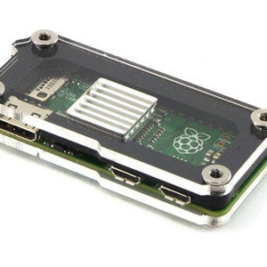 Pode incluir: Uma caixa transparente de acrílico para um computador Raspberry Pi. A caixa tem um interior preto e um dissipador de calor prateado. O logotipo do Raspberry Pi é visível na placa de circuito.