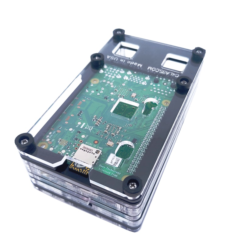 May include: A clear plastic case with black accents for a Raspberry Pi computer. The case is made in the USA and has the text "COM Made in USA" printed on it.