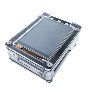 May include: A clear plastic case with a black screen inside. The screen is a small LCD display with a black border. The case has a few screws on the side.
