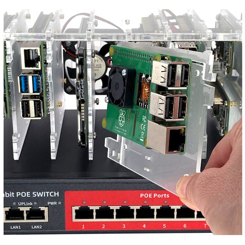 May include: A clear acrylic case with a Raspberry Pi computer board inside. The board has a green circuit board with a black fan and a black and white Raspberry Pi logo. The case has a black base with a red label that says "bit POE SWITCH" and has a row of eight ethernet ports labeled "POE Ports".