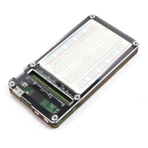 Peut inclure: Un boîtier en acrylique noir avec un dessus transparent, conçu pour contenir un Raspberry Pi et une platine à pain. Le boîtier dispose d'un port USB et d'un emplacement pour carte micro SD. La platine à pain est blanche avec des lignes rouges et bleues.